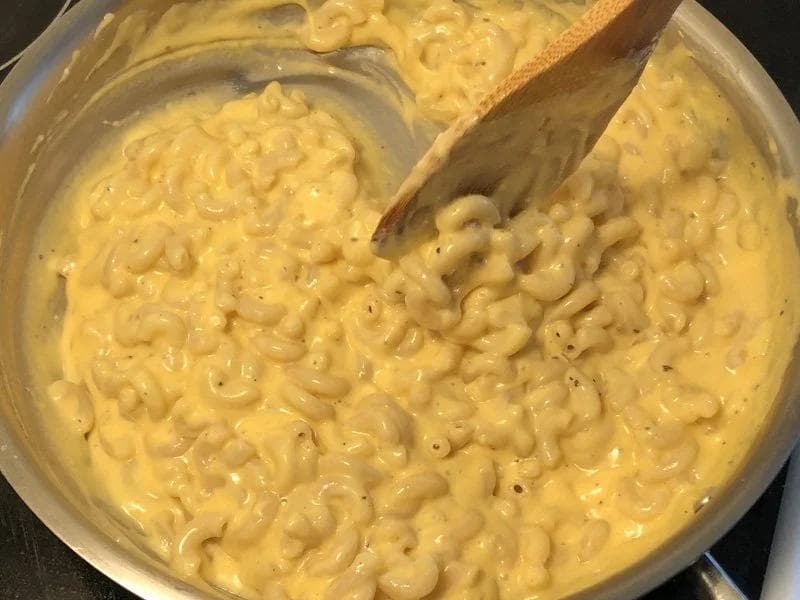 Creamy mac and cheese being stirred in a pot with a wooden spoon, showing elbow pasta coated in yellow cheese sauce.