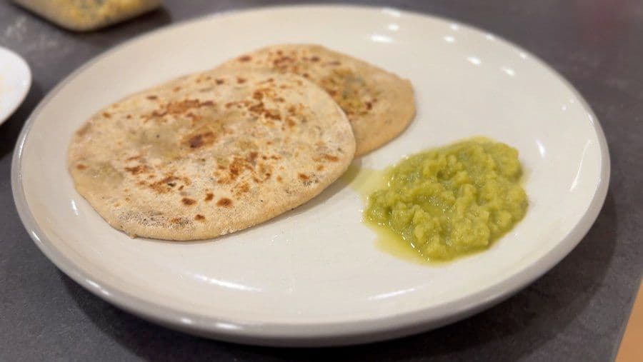 Whole wheat flatbreads served with bright green amla chutney on a white plate.