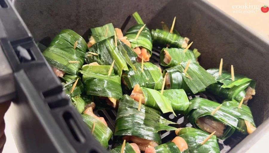 Pandan-wrapped chicken pieces secured with toothpicks, arranged in a single layer in an air fryer basket before cooking.