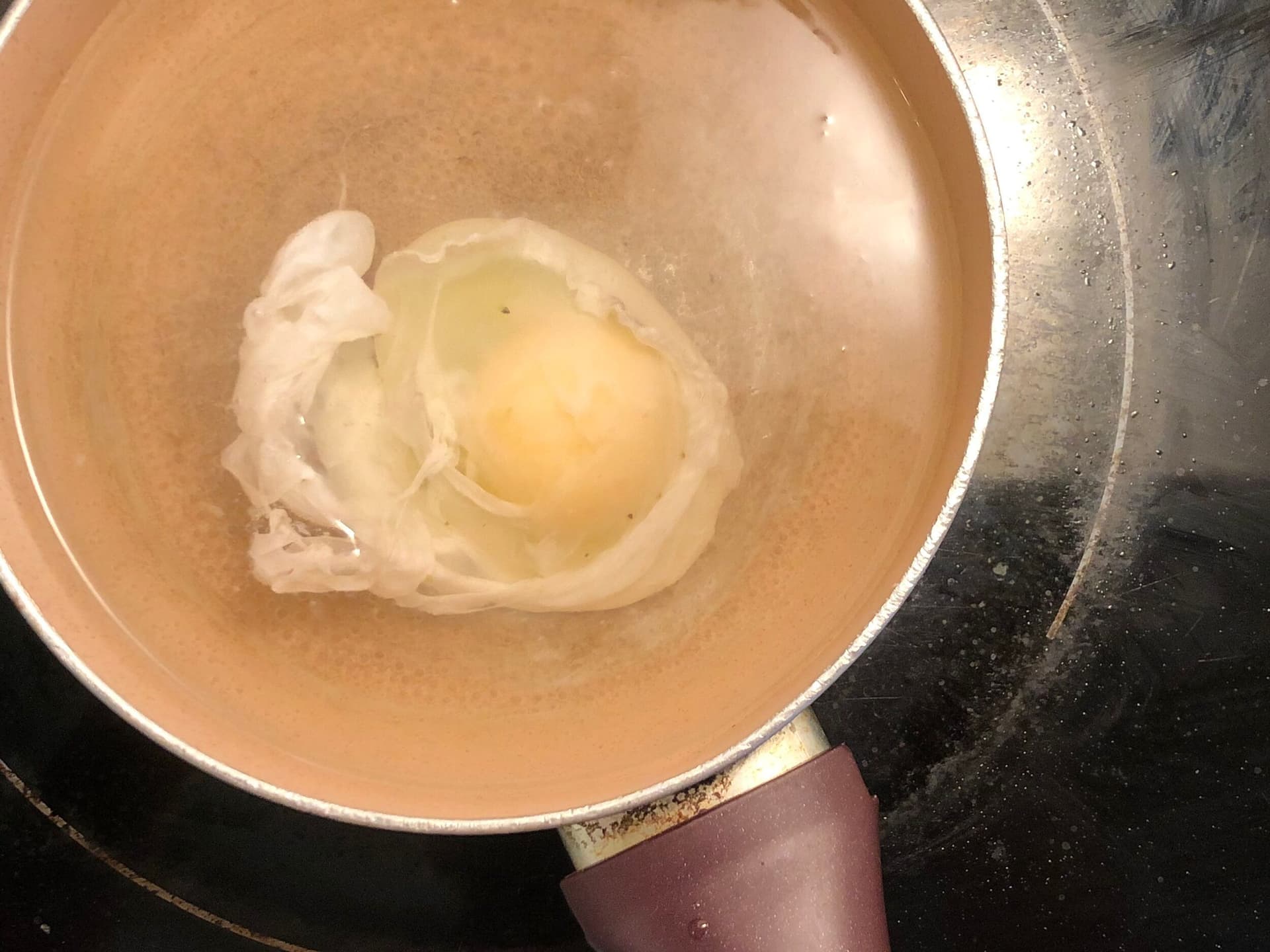 Poached egg in simmering water with white cooked around golden yolk in terracotta pot.
