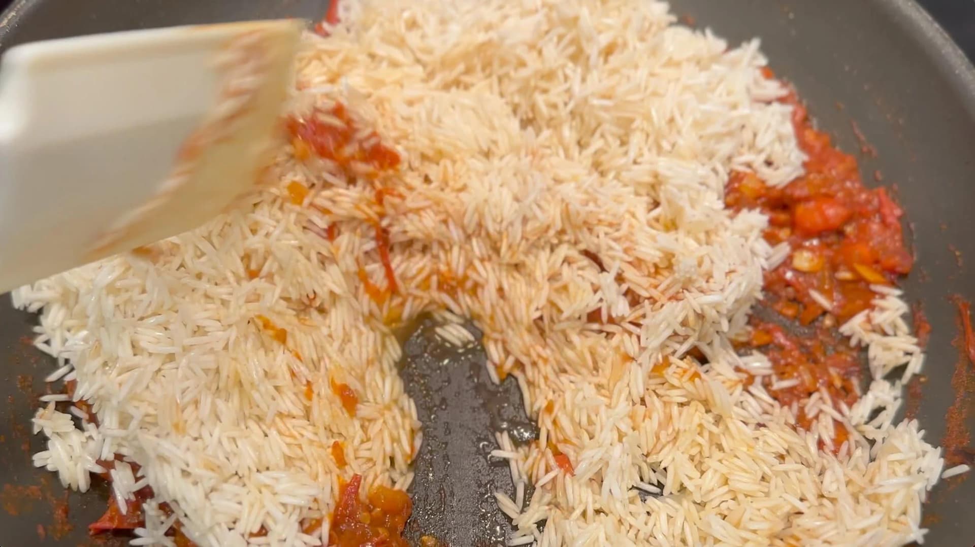 Rice and tomato mixture being stirred in a pan with a wooden spoon during preparation.
