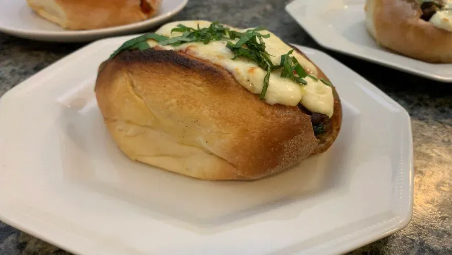 Toasted meatball sub sandwich topped with melted cheese, fresh basil, and diced mozzarella on a white plate.