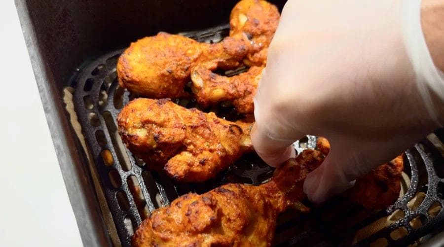 Butter being brushed onto golden-brown tandoori chicken pieces on an air fryer rack.