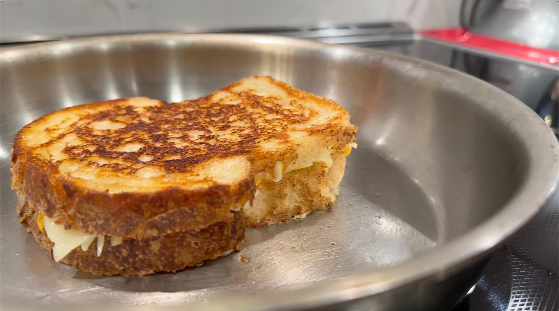 Golden brown grilled cheese sandwich with melted cheese visible on the sides, cooking in a stainless steel pan.