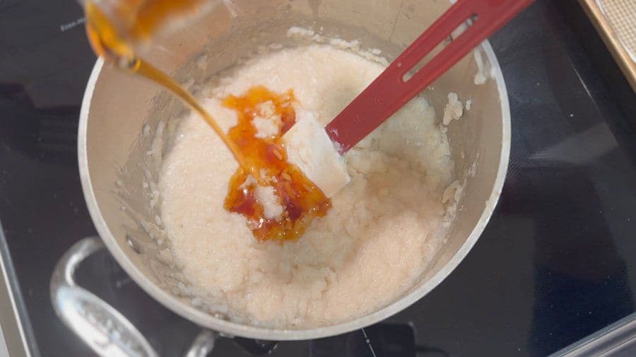 Golden cinnamon and nutmeg being stirred into creamy rice pudding in a white bowl with a red spoon.