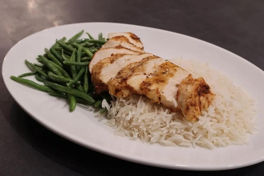 Sliced air fryer chicken breast served over white rice with green beans on a white plate.