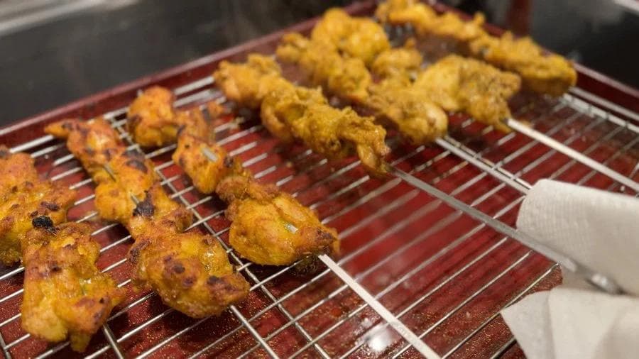 Chicken satay skewers on a wire rack during broiling, golden and charred on one side.