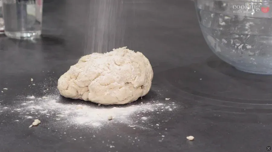 Smooth dough ball flattened on a dark work surface dusted with flour, ready to be rolled out for bhature.