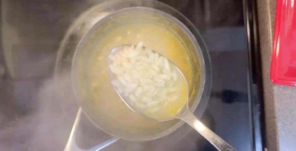 Cooked rice being spread on parchment paper with a spoon for cooling before frying.
