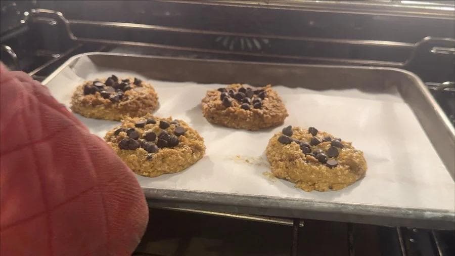 Four pumpkin chocolate chip cookies on parchment paper in a baking tray, fresh from the oven.