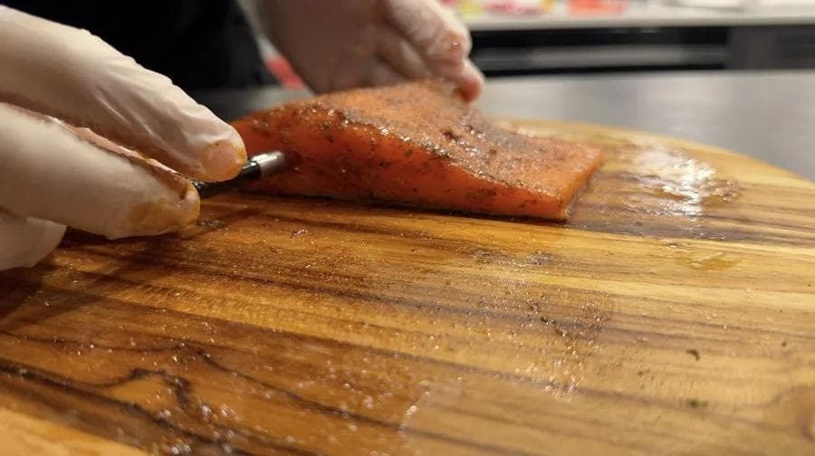Hand rubbing spices onto raw salmon fillet on wooden cutting board