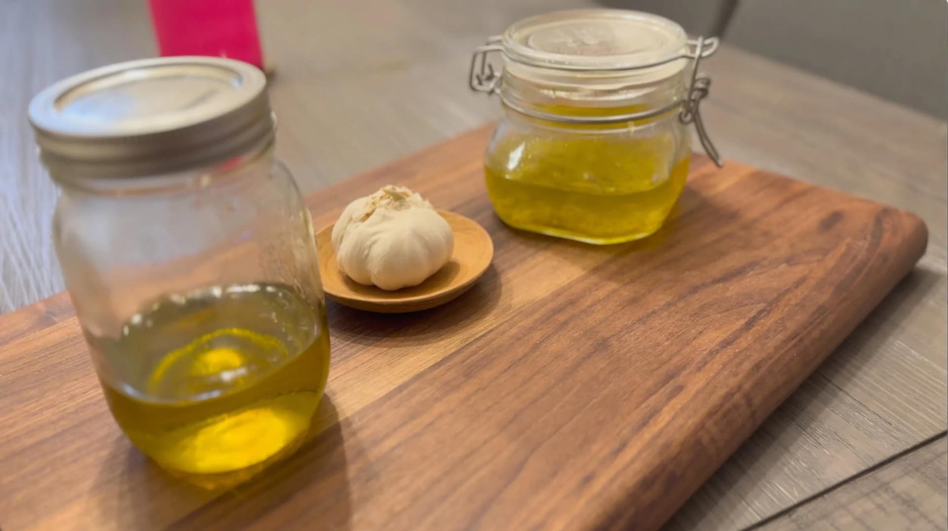 Homemade garlic-infused oil in glass jars and a squeeze bottle with fresh garlic clove on wooden board.