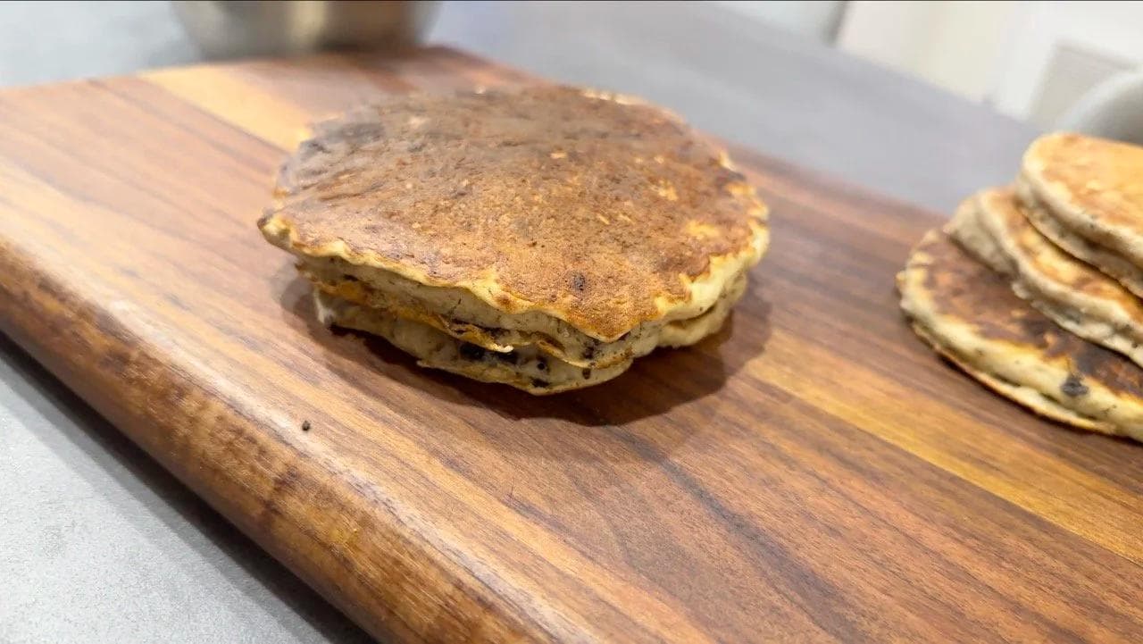 Stacked gluten-free pancakes with cream cheese glaze and crushed Oreos on a wooden board.