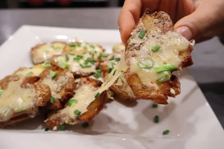 Crispy air fryer smashed potatoes topped with melted cheese and green onions on a white plate.