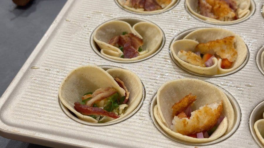 Unbaked breakfast egg cups with bacon, sausage, hash browns, and cheese in muffin tin before baking.