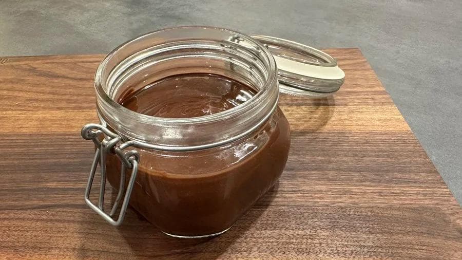Homemade chocolate hazelnut spread stored in a glass mason jar with an airtight lid on a wooden surface.