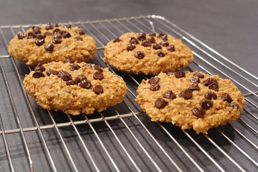 Four baked pumpkin chocolate chip cookies cooling on a wire rack.