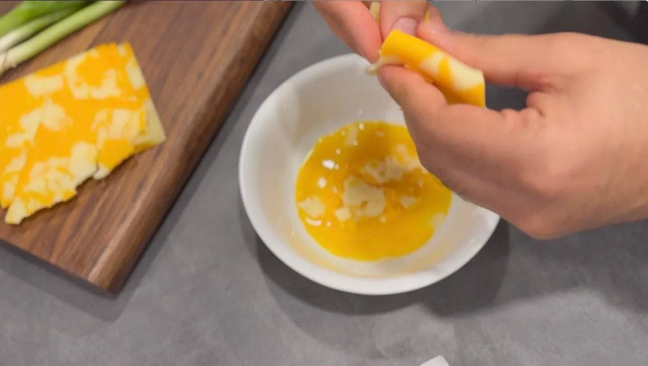 Hand squeezing egg yolk into white bowl with separated yolk, wooden cutting board with egg white nearby