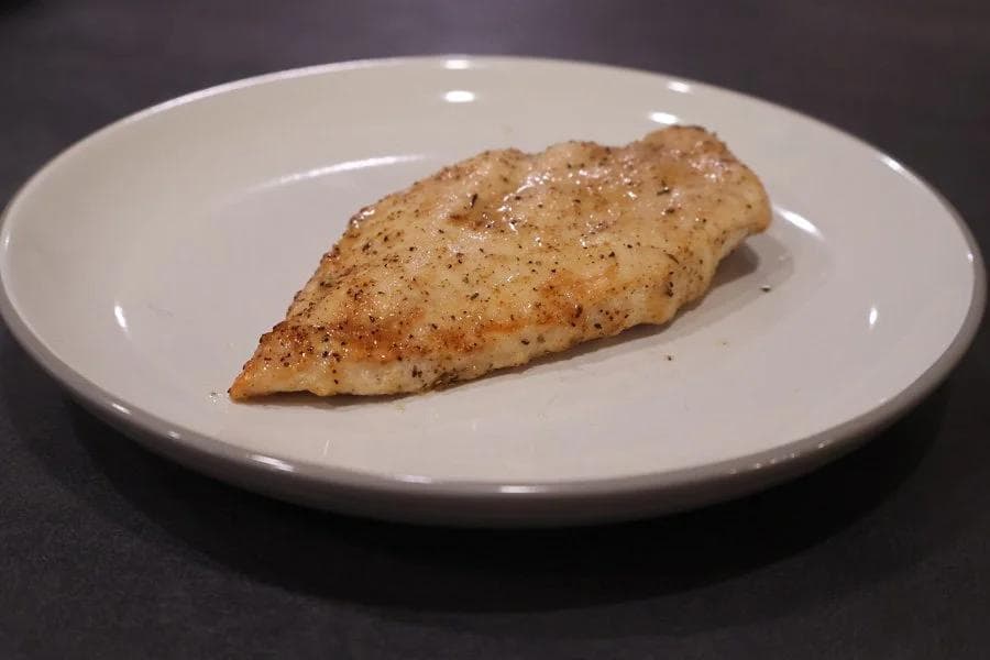 Golden-brown air fryer chicken breast seasoned with black pepper on a white plate.