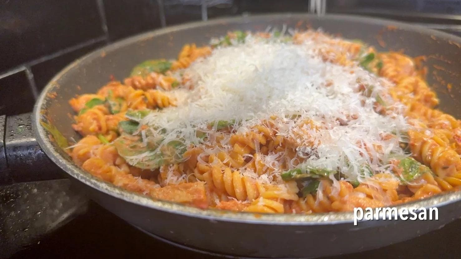 Creamy tomato pasta with diced chicken, spinach, and fresh parmesan cheese in a skillet, ready to serve.