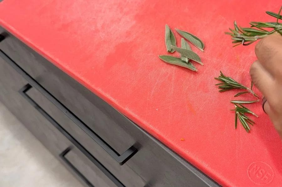 Fresh rosemary sprigs chopped on a red cutting board next to minced garlic.