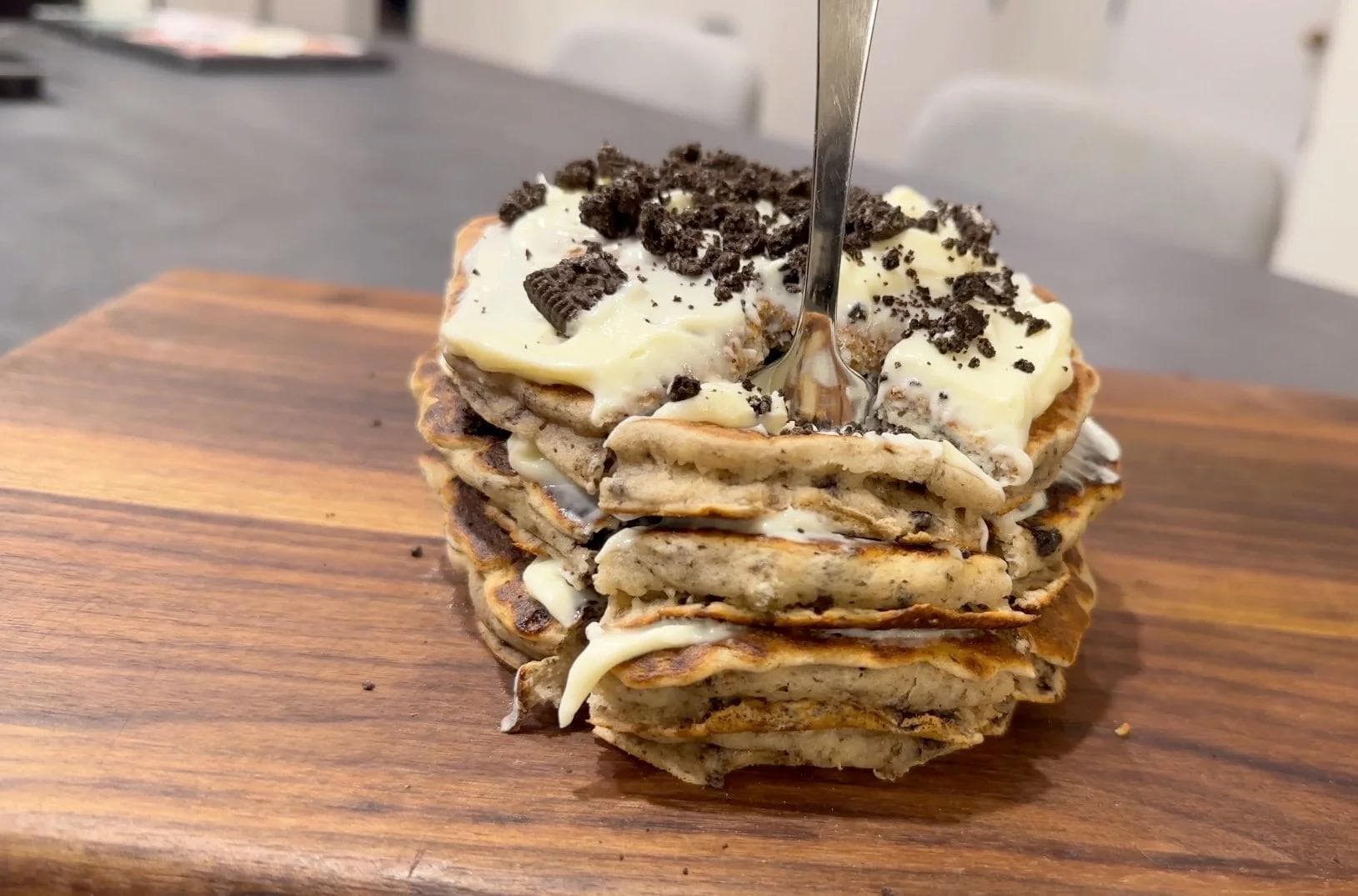 Stack of gluten-free Oreo cheesecake pancakes topped with whipped cream and crushed cookies, with a fork inserted.