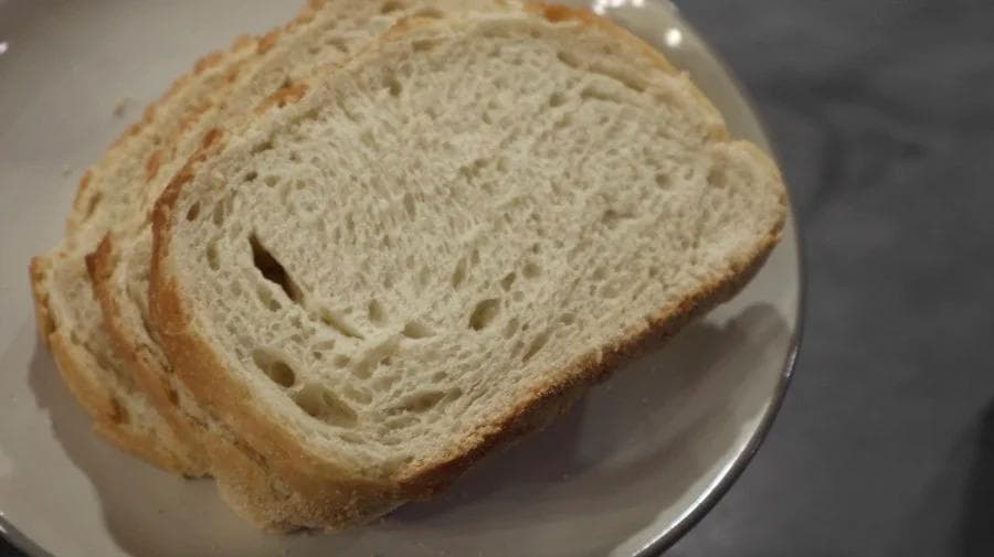 Sliced white bread with airy crumb structure on a white plate, showing breadcrumb texture for coating.