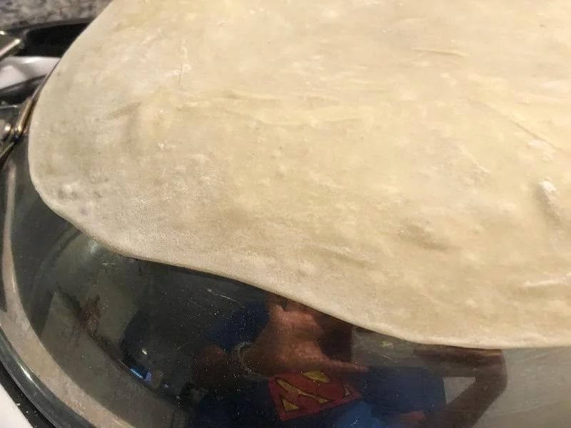 Rumali roti being cooked on the back of a wok, patted down with a kitchen towel to develop brown spots.