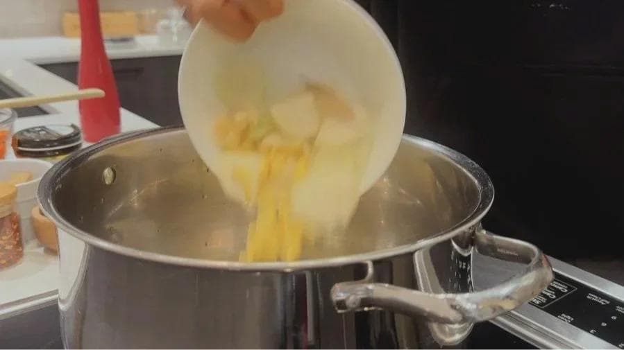 Pouring cooked onions and ginger into a large stainless steel pot during soup preparation.