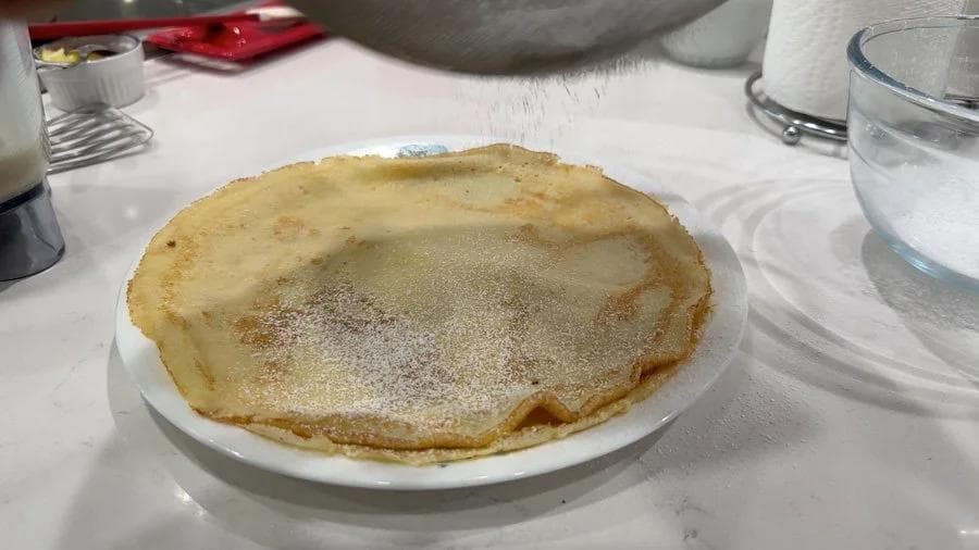 Single gluten-free lemon mascarpone crepe dusted with powdered sugar on a white plate.