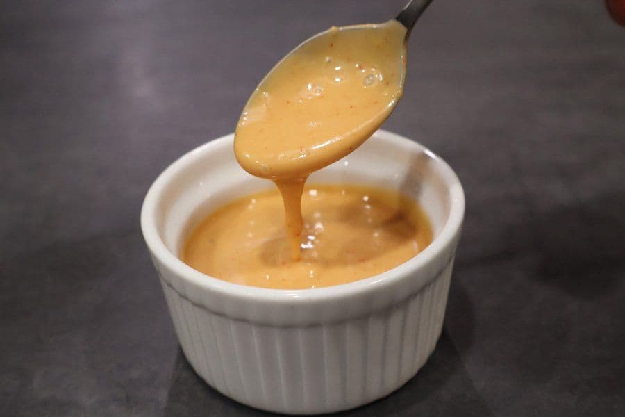 Spicy umami sauce being drizzled from a spoon into a white bowl, showing its creamy, smooth texture.