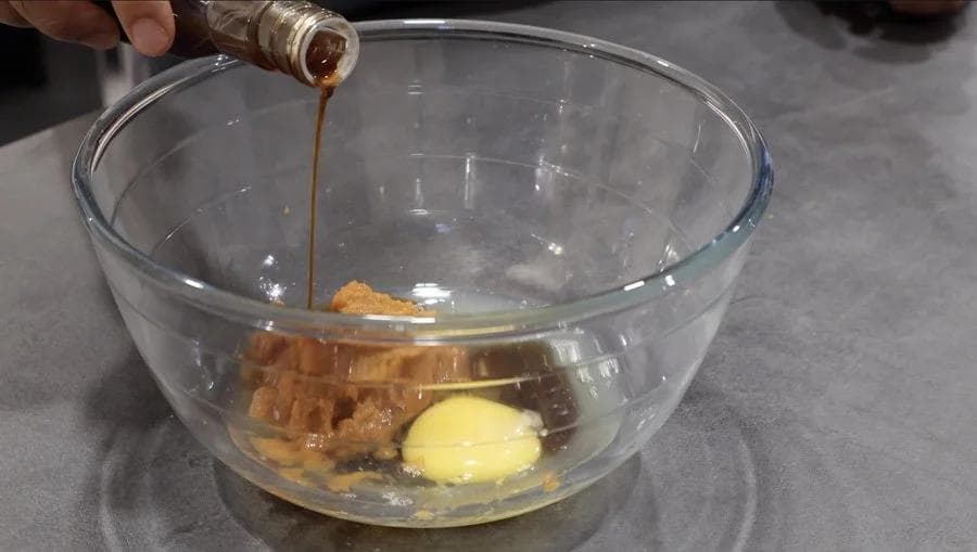 Pouring maple syrup into a glass bowl containing pumpkin puree, egg, and other wet ingredients for cookie batter.