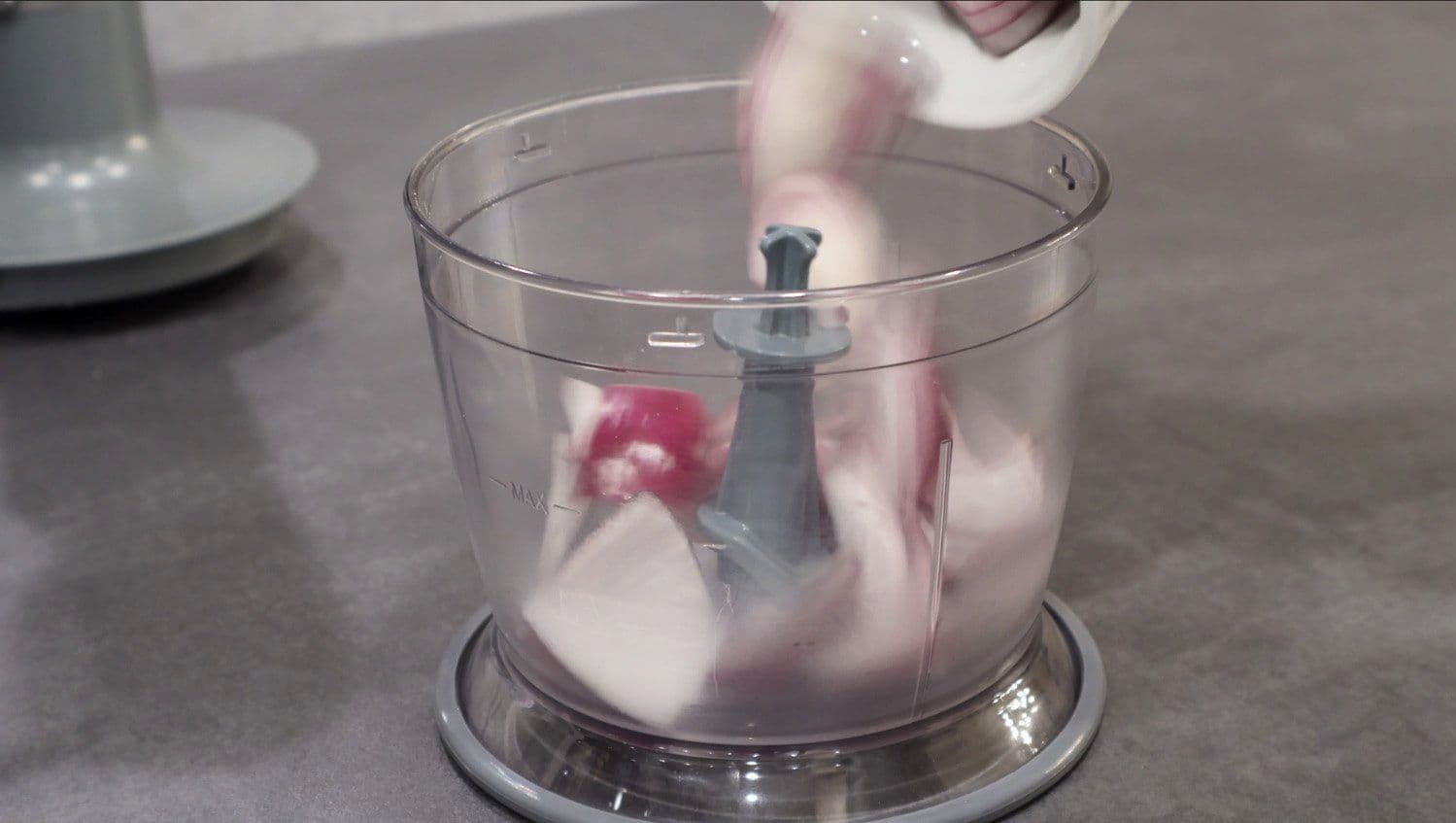 Pouring liquid into food processor containing ginger, garlic, and onion for Rajma Masala paste.