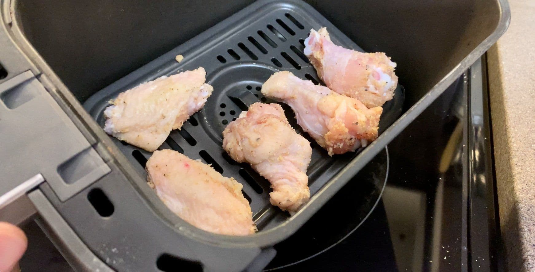 Raw chicken wings seasoned with garlic powder and flour in an air fryer basket before cooking.
