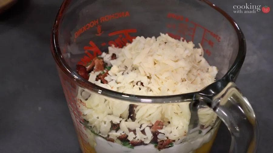 Egg mixture with cottage cheese, bacon, and herbs combined in a measuring cup, ready to pour into muffin tins.