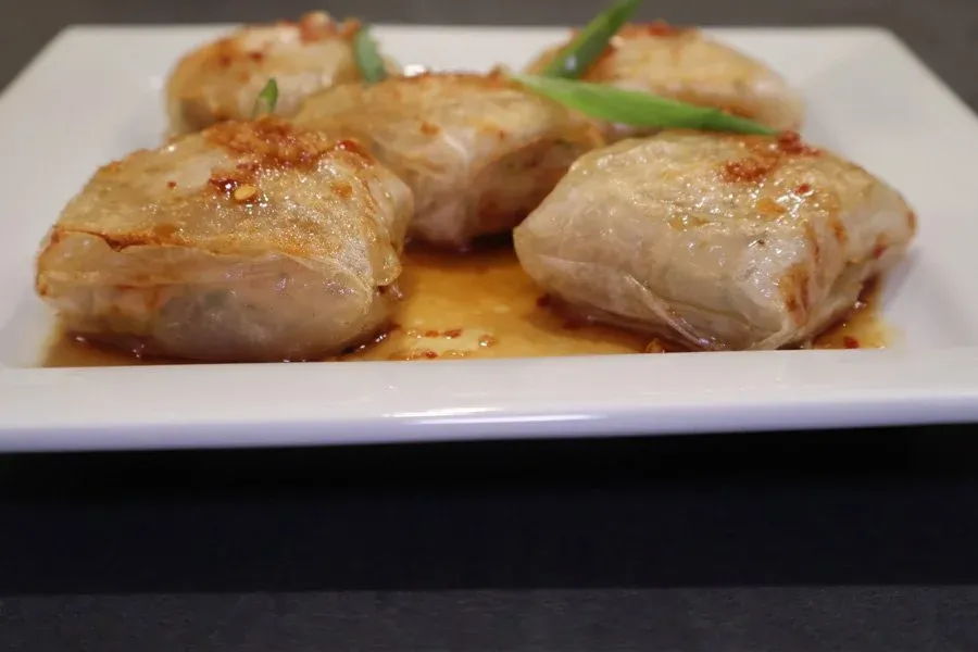 Five golden-brown air fryer chicken dumplings on a white plate with stir fry sauce and green onion garnish.
