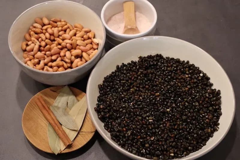 Ingredients for dal makhani: black lentils, kidney beans, bay leaf, cinnamon stick, and spices in white bowls.