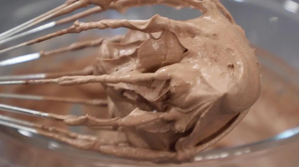 Chocolate whipped cream at soft peak stage clinging to whisk wires over a bowl