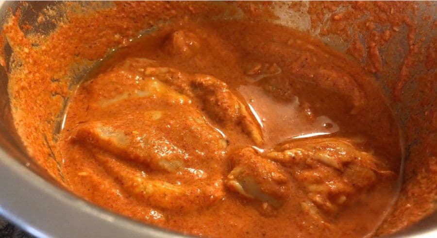 Rich orange-red chicken tikka marinade in a bowl, showing tender marinated chicken pieces coated in creamy yogurt-based sauce.