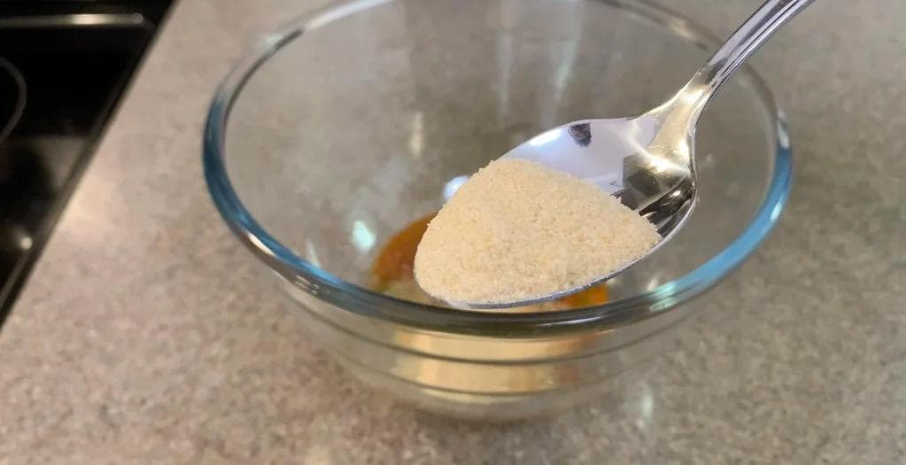 Spoon holding seasoned marinade mixture over glass bowl with oil and spices for arroz con pollo