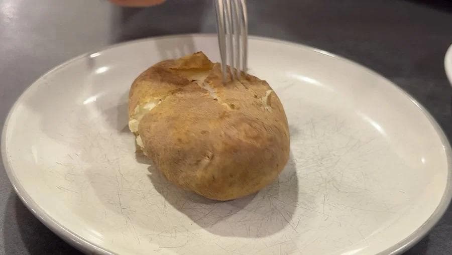 Air-fried baked potato with fork piercing soft skin on white plate, demonstrating texture without foil wrapping.