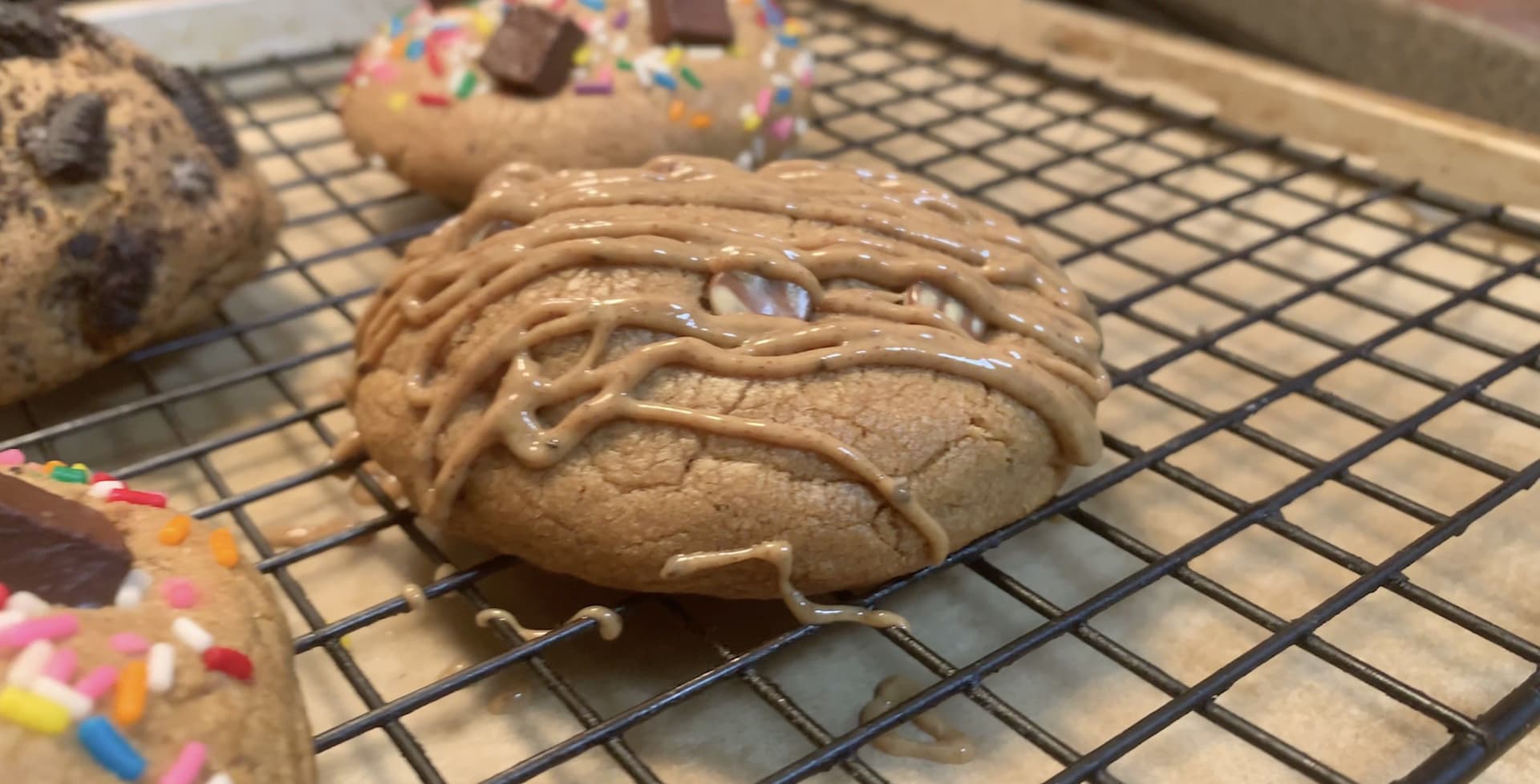 Peanut butter stuffed chocolate chip cookies cooling on a wire rack, drizzled with peanut butter.