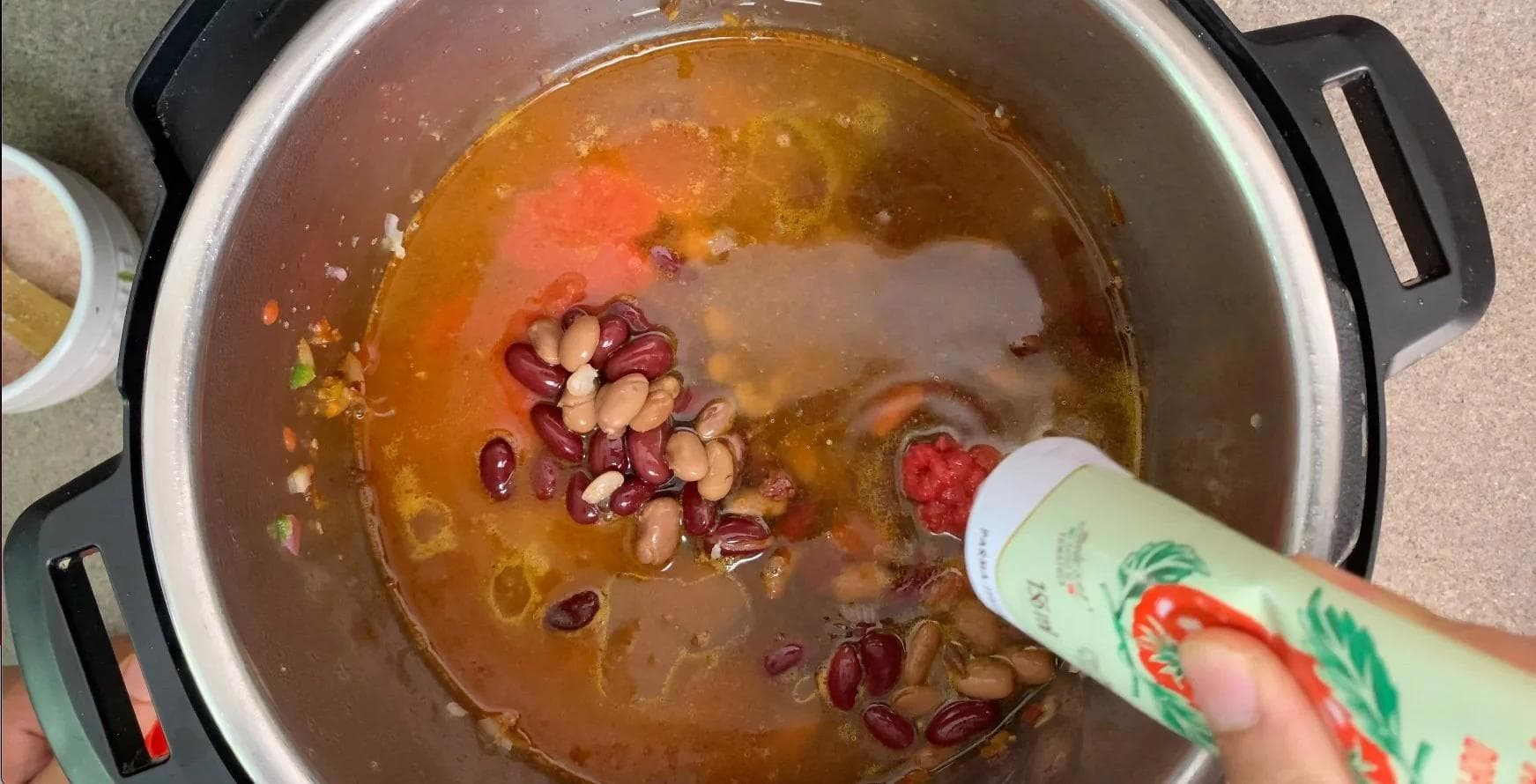 Instant Pot chili with red kidney beans and pinto beans being stirred into broth and tomato-based sauce.