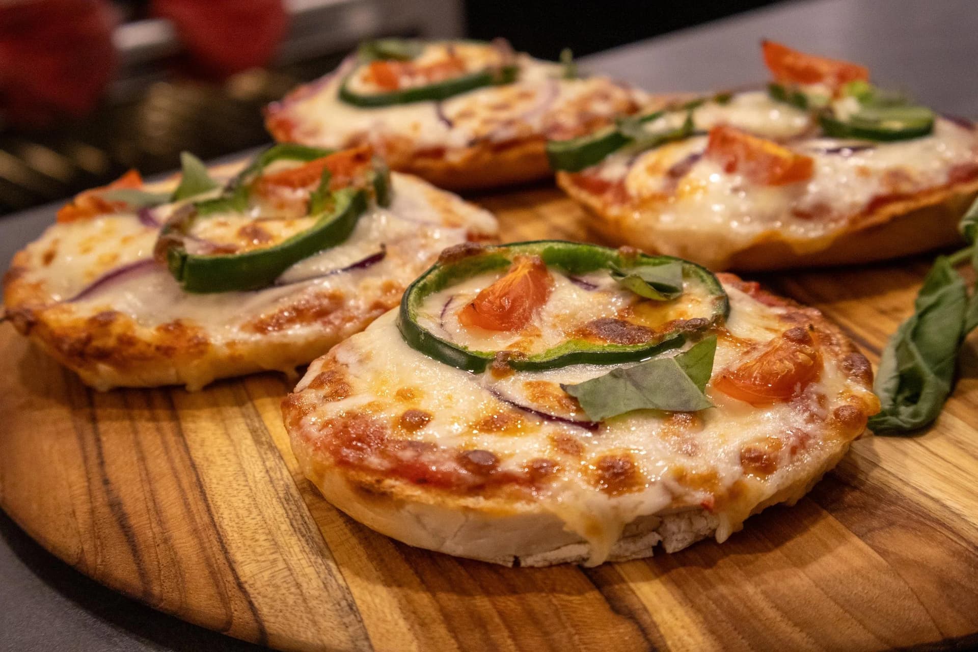 Baked veggie pizza bagels topped with melted cheese and fresh jalapeño slices on a wooden board.