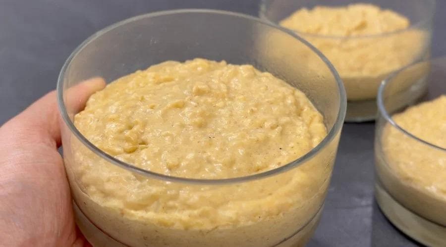 Creamy pumpkin rice pudding in clear serving glasses with a spoon lifting a portion to show the thick, custard-like texture.