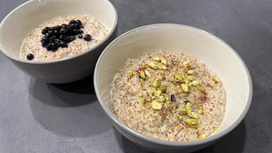 Two bowls of creamy cracked wheat porridge topped with blueberries and pistachios.