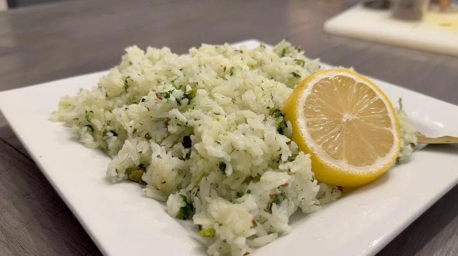 Cilantro lemon rice garnished with fresh herbs on a white plate with a lemon slice beside it.