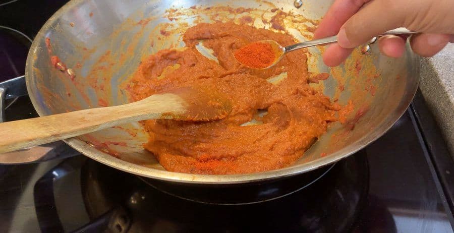 Spiced ginger-cilantro masala paste cooking in a wok, being stirred with a wooden spoon.