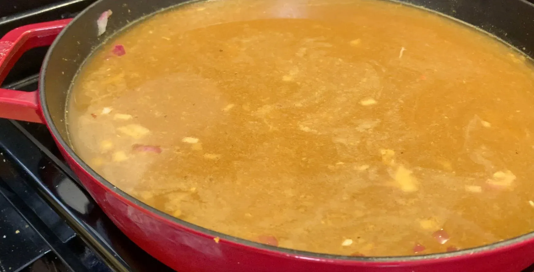 One-pot Moroccan stew simmering in a red Dutch oven with golden broth and visible chicken pieces.