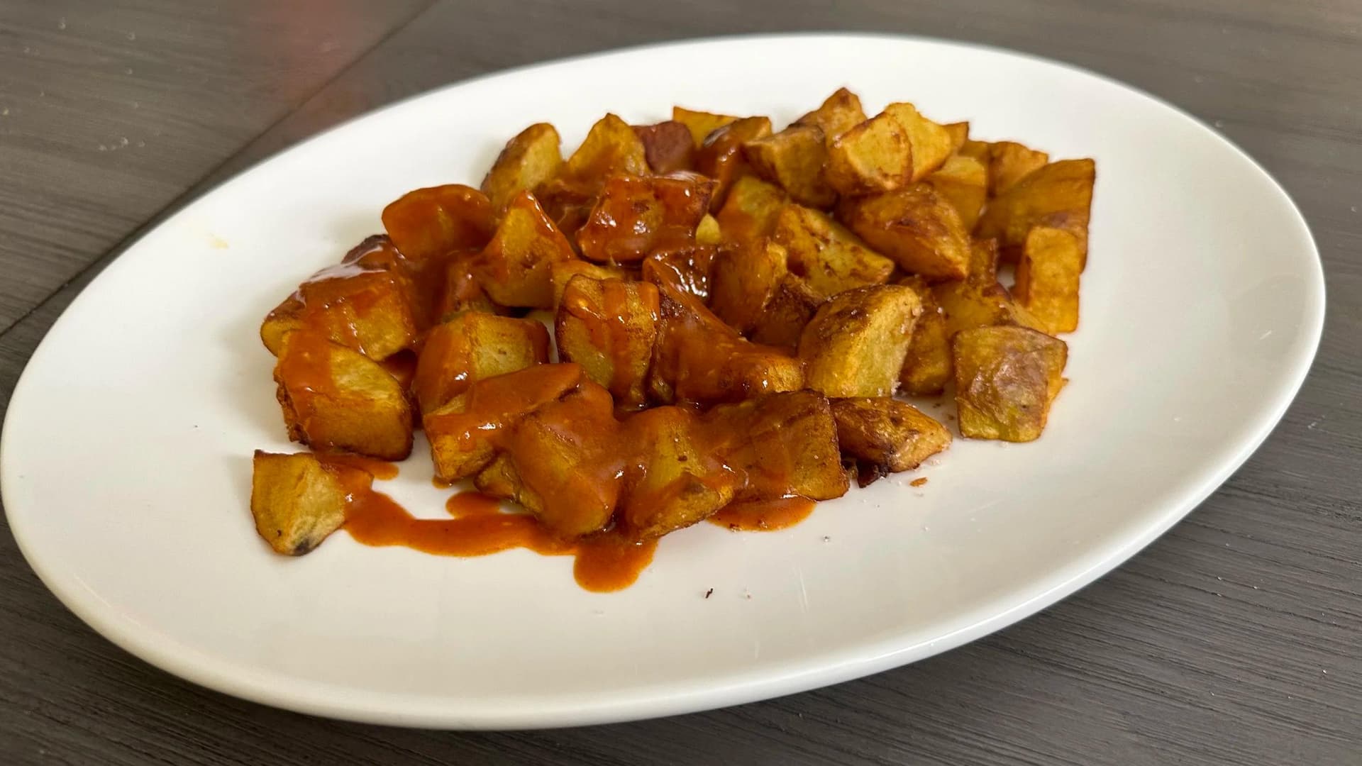 Crispy golden cubed potatoes with spicy red sauce on a white plate, Spanish Patatas Bravas.